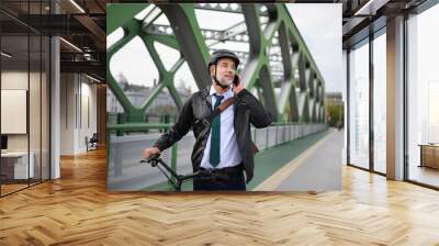 Portrait of businessman commuter on the way to work, pushing bike and calling on mobile phone, sustainable lifestyle concept. Wall mural