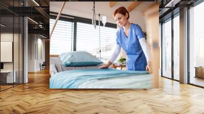 Portrait of female nurse or housekeeping staff changing sheets in hospital. Wall mural