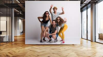 Portrait of joyful young group of friends with hat and sunglasses standing in a studio. Wall mural