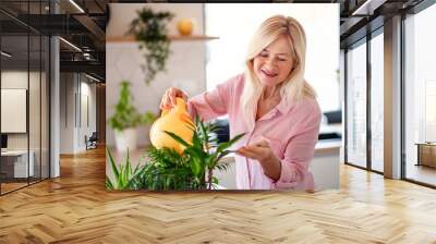 Portrait of senior woman watering plants indoors at home. Wall mural