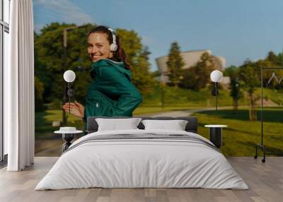 Portrait of smilling young woman with headphones running in the city park in the early morning. Wall mural