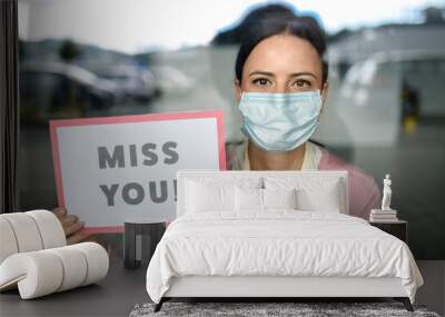 Portrait of teacher with face mask after lockdown, holding miss you sign. Wall mural