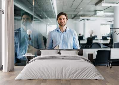 Portrait of young businessman standing in an office, looking at camera. Wall mural