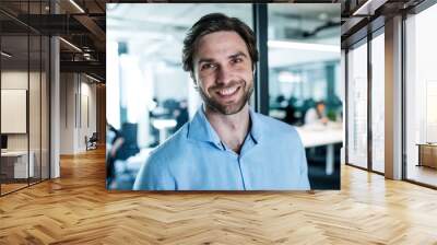 Portrait of young businessman standing in an office, looking at camera. Wall mural