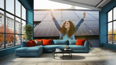 Portrait of young excited woman on roof with solar panels. Wall mural