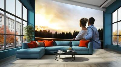 Rear view of couple standing on patio of wooden cabin at sunset, holiday in nature concept. Wall mural