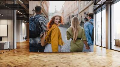 Rear view of group of happy young people outdoors on trip in town, walking and looking back. Wall mural