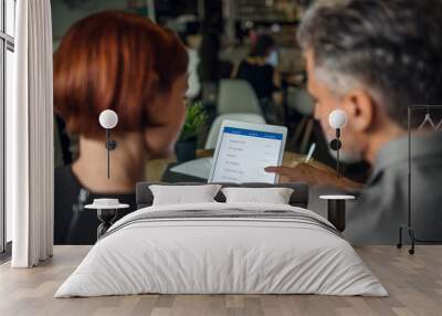 Rear view of man and woman having business meeting in a cafe, using tablet. Wall mural