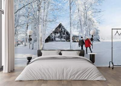 Rear view of young couple walking outdoors in snow in winter forest. Wall mural