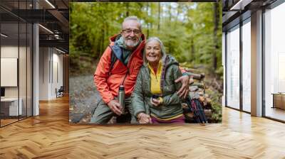 Senior couple having break during hiking in autumn forest. Wall mural