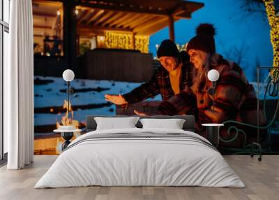 Senior couple sitting and heating together at outdoor fireplace in winter evening. Wall mural