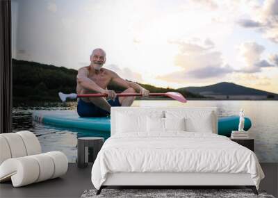 Senior man sitting on paddleboard on lake in summer. Copy space. Wall mural