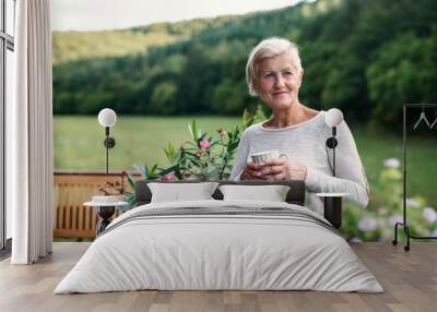 Senior woman with coffee standing outdoors on a terrace in summer. Wall mural