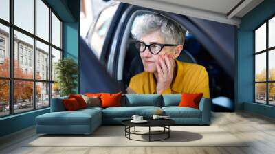 Senior woman with glasses getting out of a car. Wall mural