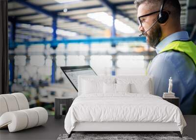 Side view of technician or engineer with headset and laptop standing in industrial factory. Wall mural