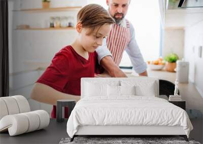 Small boy with father indoors in kitchen, learning how to make pancakes. Wall mural