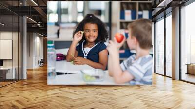 Small school children sitting at the desk in classroom, eating fruit. Wall mural