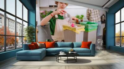 Teen girl throwing plastic bottles in recycling bin in the kitchen. Wall mural