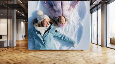 Top view portrait of cheerful mother with small daughter lying in snow in winter nature. Wall mural