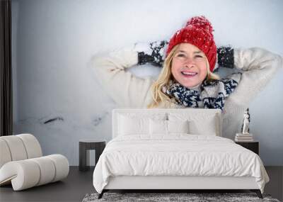 Top view portrait of senior woman with hat outdoors lying on snow, looking at camera. Wall mural