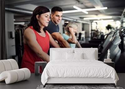 Two cheerful female seniors in gym with a young trainer doing cardio work out. Wall mural