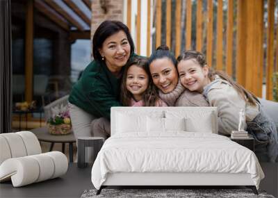 Two happy sisters with mother and grandmother embracing and looking at camera outdoors in patio in autumn. Wall mural