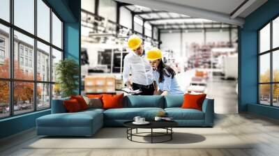 Two project managers standing in modern industrial factory, looking blueprints and documents on table. Manufacturing facility with robotics, robotic arms and automation. Storing products and materials Wall mural