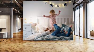 Two small children jumping on bed indoors at home, having fun. Wall mural