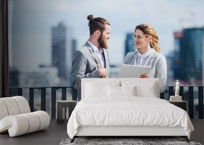 Two young business people with tablet standing on a terrace outside office, working. Wall mural