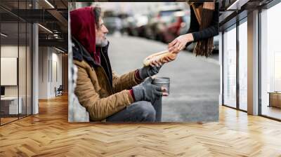 Unrecognizable woman giving food to homeless beggar man sitting in city. Wall mural