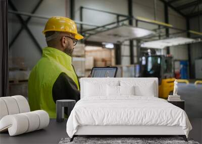 Warehouse receiver standing by delivered cargo, holding tablet, looking at cargo details, checking delivered items, goods against order. Wall mural