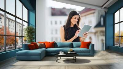 Young businesswoman with tablet standing on a terrace outside an office in city. Wall mural