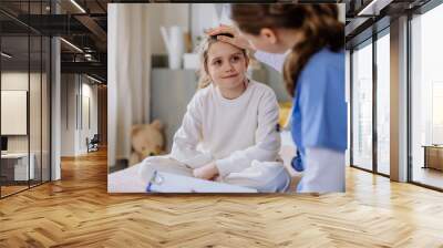 Young doctor taking care of little girl in hospital room. Wall mural