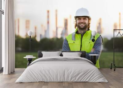 Young engineer standing outdoors by oil refinery, looking at camera. Wall mural