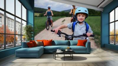 Young family with little child riding bicycles on road in village in summer. Wall mural