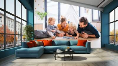 Young family with two small children indoors in bedroom reading a book. Wall mural