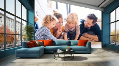 Young family with two small children indoors in bedroom reading a book. Wall mural