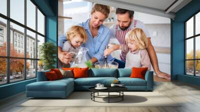 Young family with two small children indoors in kitchen, cooking. Wall mural