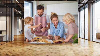 Young family with two small children indoors in kitchen, eating pancakes. Wall mural