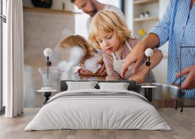 Young family with two small children indoors in kitchen, preparing food. Wall mural