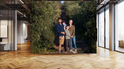 Young family with two small children standing outdoors by olive trees. Wall mural