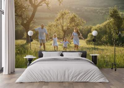 Young family with two small children walking on meadow outdoors at sunset. Wall mural