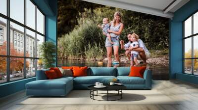 Young family with two toddler children outdoors by the river in summer, playing. Wall mural