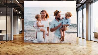 Young family with two toddler children walking on beach on summer holiday. Wall mural