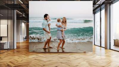 Young family with two toddler children walking on beach on summer holiday. Wall mural