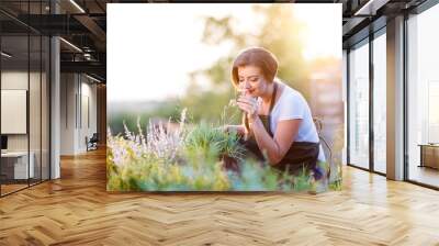 young gardener in garden smelling flower, sunny nature Wall mural