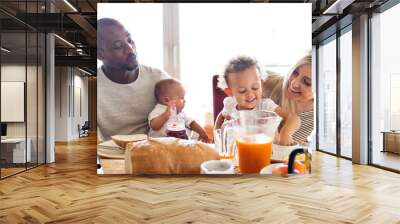 Young interracial family with little children having breakfast. Wall mural