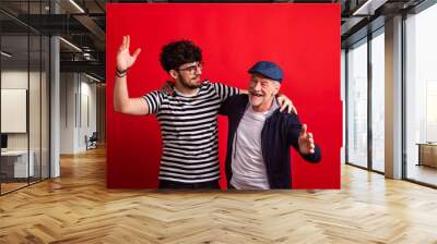 Young man and senior father in a studio on red background. Wall mural