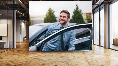 Young man with blue shirt and tie getting out of car in town. Wall mural