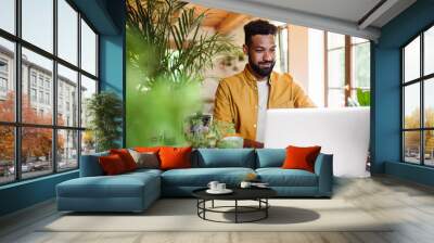 Young man with laptop and coffee working indoors, home office concept. Wall mural